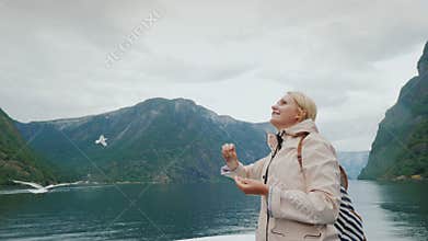 Happy woman feeds a seagull on a cruise through the fjords of Norway