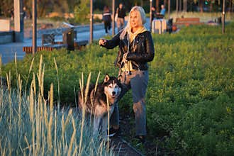 A blonde girl of European appearance with a husky dog walks on the sea promenade on a summer evening after the rain