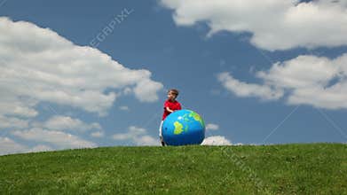 boy rolling inflatable ball on meadow towards to