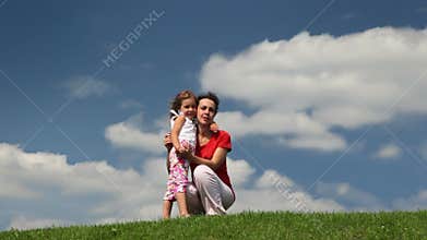 mother and daughter squat on meadow embracing,