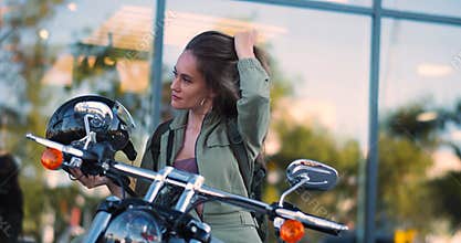 A young beautiful Caucasian biker woman takes off her helmet and shakes her hair.