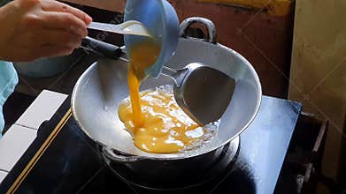 Pouring mixed egg or beaten egg or whisked egg into the frying pan on the lit black stove.