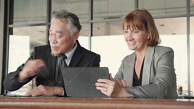 Two senior business man and woman in formal meeting and discussing documents and using a tablet in modern office.
