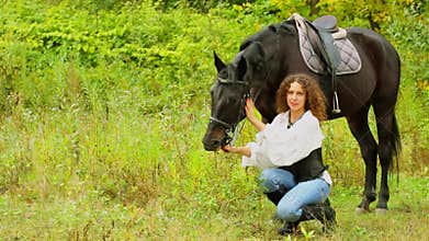 Handsome woman sits and holds chestnut horse at