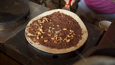 Making of crispy crepe filled with nutella and cashew nuts on crepe stove