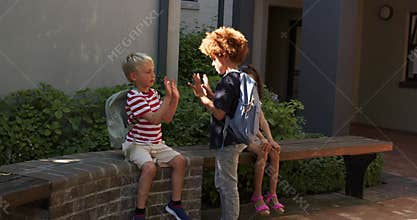 Kids watching standing boy reaching out, two boys with backpacks greeting with high-fives at school