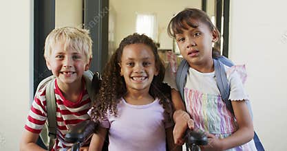 Diverse school-age children posing for camera in entry, leaning toward wheelchair with backpacks