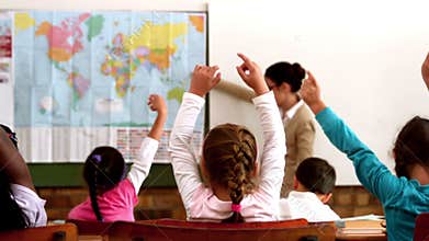 Young pupils raising hands during geography lesson in classroom
