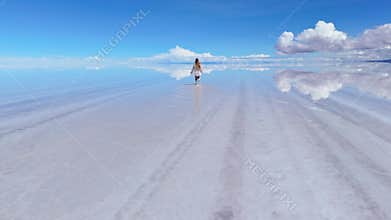 A woman walks across the expansive Salar de Uyuni salt flats in Bolivia, her reflection mirrored in the shallow water