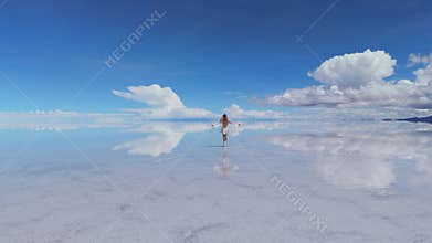 A woman walks across the expansive Salar de Uyuni salt flats in Bolivia, her reflection mirrored in the shallow water under a