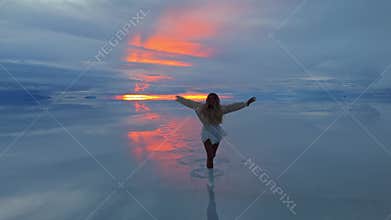 A woman running across the Salar de Uyuni salt flats in Bolivia during a stunning sunset