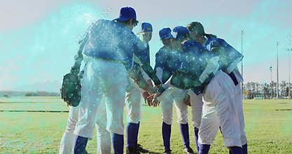 Huddling seven women leaning in on grassy field, showing baseball glove, caps, blue jerseys, cleats