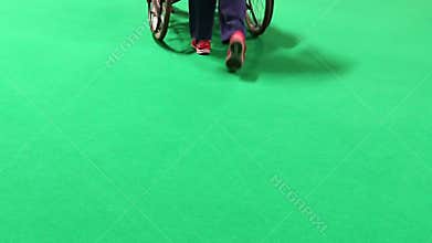 Woman pushing wheelchair isolated on green
