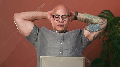 Focused Bald Man With Glasses Working On Laptop Takes A Relaxing Break