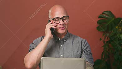 Happy Business Man Smiling During a Phone Call While Working on His Laptop