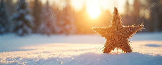 A straw star decoration rests in soft snow with a bright sun setting behind a blurred forest. This festive, rustic scene offers a
