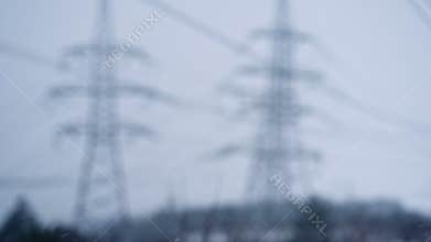 Electric voltage towers blurry background. Power line, electricity pylons. Winter snowflakes.