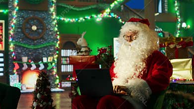 Man portraying Christmas character amused by children wish lists on laptop
