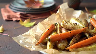 A rustic and autumnal food display showcases roasted carrots, parsnips, and potatoes on parchment paper, with fall leaves and