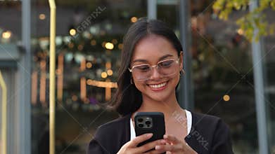 Portrait of Asian woman in glasses takes selfie on smartphone and smiles in city