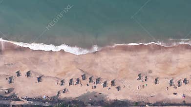Top-down aerial view of traditional fishing boats arranged in rows on a sandy beach as a wave breaks on the shore in India
