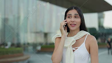 Portrait of Brazilian woman talks on smartphone and stands near office building