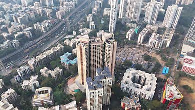 Aerial shot of a Mumbai suburb showing a high-rise with solar panels, an adjacent slum, and a busy highway