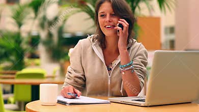 Smiling student studying in the canteen then answering her phone