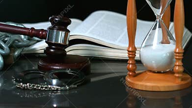 Gavel and handcuffs dropping onto sounding block beside hourglass and bible