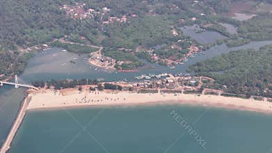 Aerial drone flight from Sagareswar Beach, over a bustling fishing harbor with a bridge, towards the town of Vengurla in