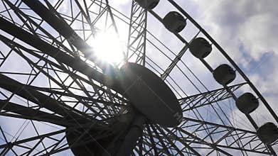 Ferris wheel and sun in sky with clouds
