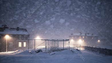 Snowstorm blankets a construction site during nighttime in a quiet urban area
