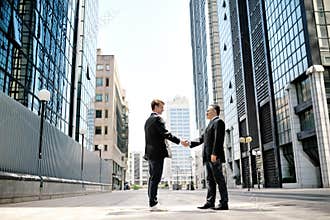 Two businessmen shaking hands on background office corporate buildings