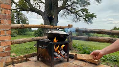 Outdoor cooking scene featuring a pot on a wood stove with a scenic landscape view