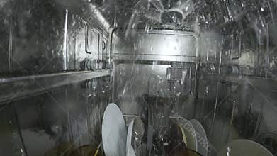 Inside view of a running dishwasher with water spraying over dishes and utensils, creating a dynamic underwater-like perspective
