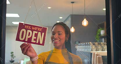 Noticing closed sign on cafe door, female barista flipping sign to open, welcoming customers