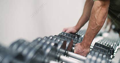 Cropped footage of a male hand picks up dumbbell from the rack.