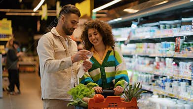 Young couple reading shopping list in supermarket aisle