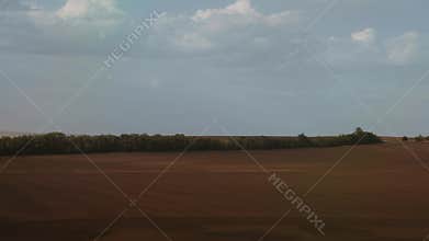 A vast, flat countryside landscape from a moving train. A dirt road cuts through harvested fields under a pale sky. Expansive and