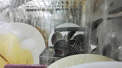 Inside view of a running dishwasher with water spraying over dishes and utensils, creating a dynamic underwater-like perspective