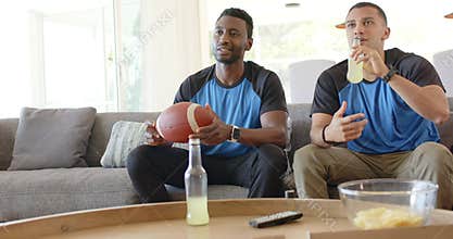 When big play flashes on TV, diverse male friends sipping lemonade and rotating football on sofa