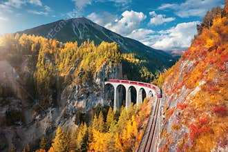 Aerial view of modern red train on Landwasser viaduct in autumn