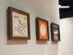 Three small, square-framed artworks hang in a descending line on a white, textured interior wall.