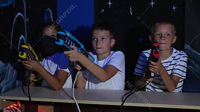 Teenage children shoot laser weapons at colored targets in the dark playroom.