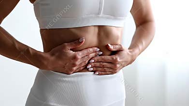 Fit woman in white sportswear holding abdomen, experiencing discomfort or stomach ache, indicating digestive issues or