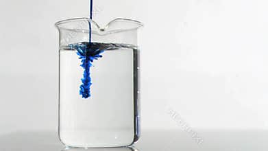 Thin blue trickle in a super slow motion flowing in a water on a beaker