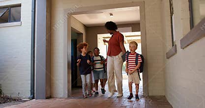 African American teacher with kids greeting boy handing tablet, leading out to yard with backpacks
