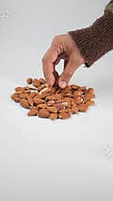 Hand reaching for almonds on a plain surface