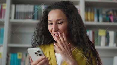 Excited delighted Latina Hispanic woman using smartphone reading exam results in library smiling female student girl