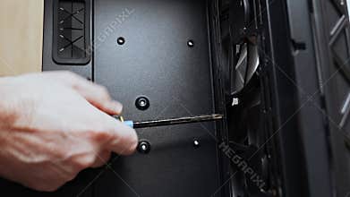 A computer technician unscrews a screw that secures a fan to a PC case. Assemble a computer system unit into a modern workstation